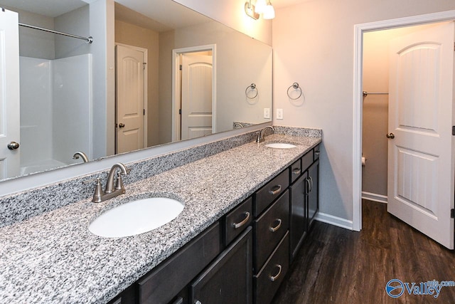 bathroom with a sink, baseboards, double vanity, and wood finished floors