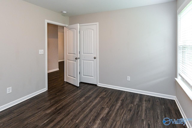 unfurnished bedroom with baseboards, multiple windows, and dark wood-type flooring