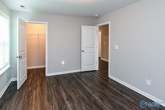 unfurnished bedroom with visible vents, dark wood-style flooring, a walk in closet, and baseboards