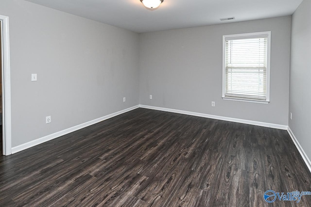 unfurnished room with baseboards, visible vents, and dark wood finished floors