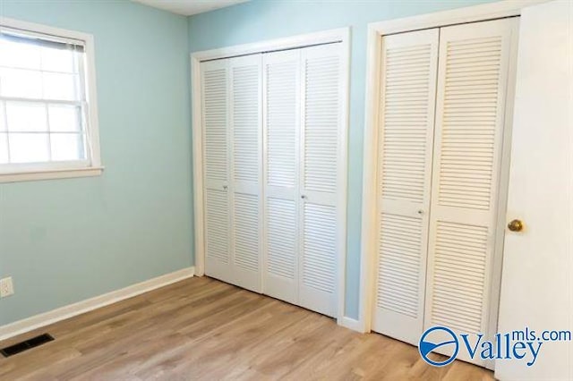 unfurnished bedroom with light hardwood / wood-style floors and two closets