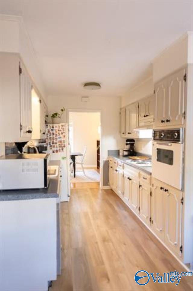 kitchen with exhaust hood, white cabinets, light hardwood / wood-style floors, and white appliances