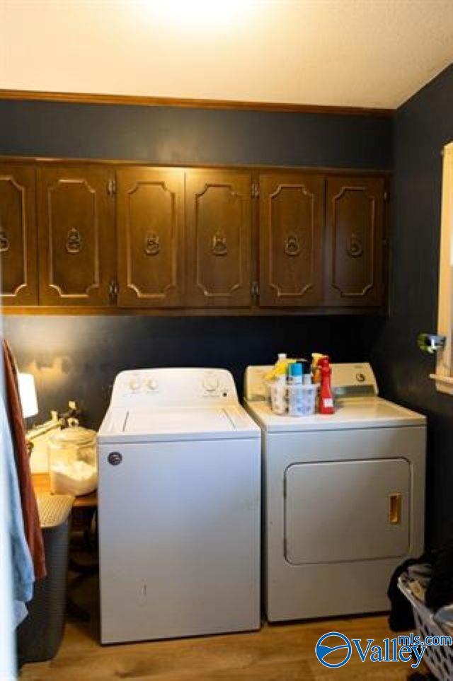 clothes washing area with washer and clothes dryer, cabinets, and light wood-type flooring