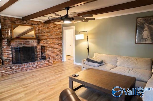 living room featuring beamed ceiling, a brick fireplace, light hardwood / wood-style flooring, and ceiling fan