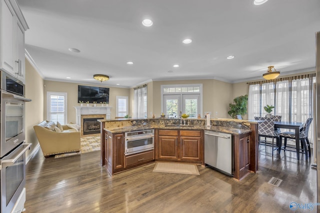 kitchen with a kitchen island with sink, crown molding, dark wood-type flooring, and appliances with stainless steel finishes