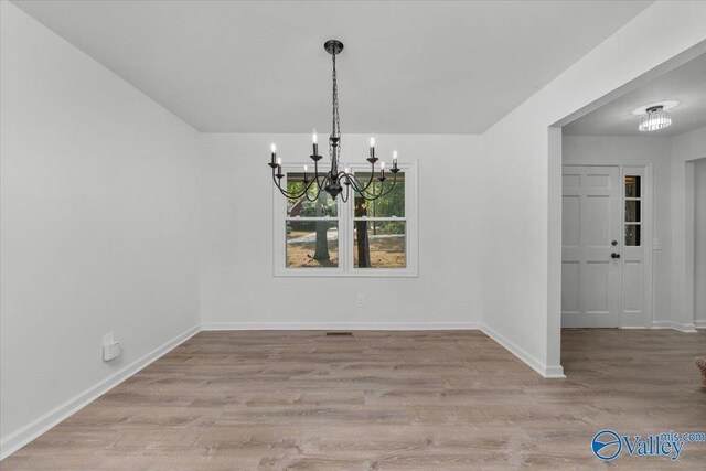 unfurnished dining area featuring a notable chandelier and light hardwood / wood-style flooring