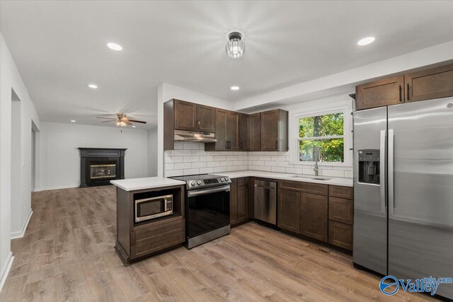 kitchen with backsplash, light wood-type flooring, appliances with stainless steel finishes, sink, and ceiling fan