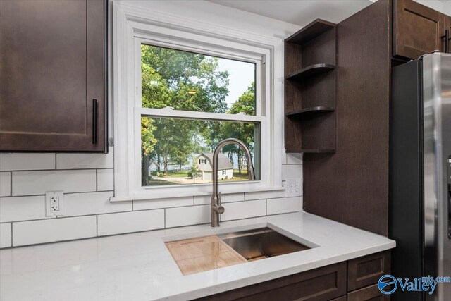 kitchen featuring stainless steel fridge, light stone counters, dark brown cabinetry, and sink