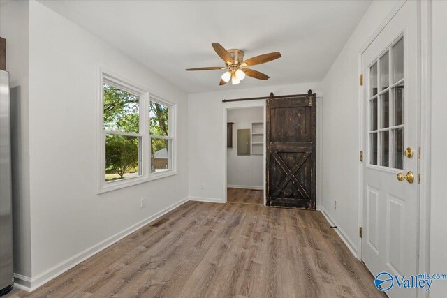 spare room with a barn door, ceiling fan, and light hardwood / wood-style floors