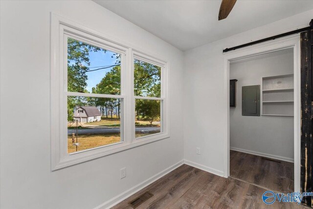 unfurnished bedroom featuring a barn door, ceiling fan, electric panel, and dark hardwood / wood-style floors