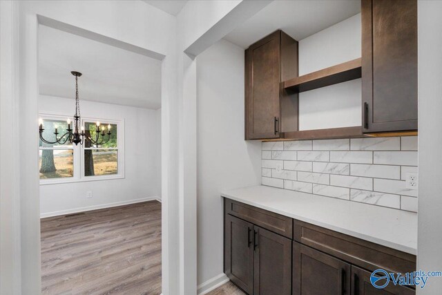 kitchen with hanging light fixtures, light hardwood / wood-style flooring, a notable chandelier, dark brown cabinets, and decorative backsplash