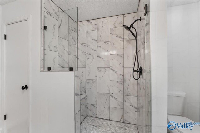 bathroom featuring toilet, a tile shower, and a textured ceiling