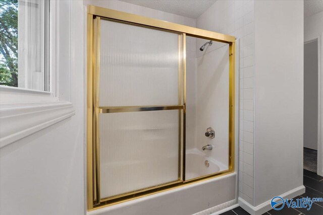 bathroom featuring a textured ceiling and combined bath / shower with glass door