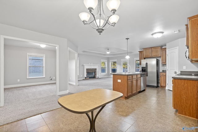 kitchen with a fireplace, decorative light fixtures, an island with sink, stainless steel appliances, and light carpet