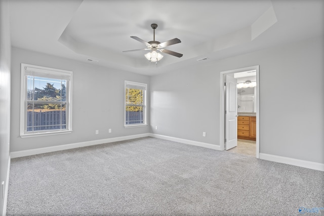 unfurnished bedroom featuring a tray ceiling, light colored carpet, ceiling fan, and ensuite bathroom