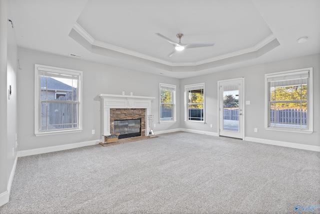 unfurnished living room featuring a tray ceiling, a fireplace, ceiling fan, and carpet