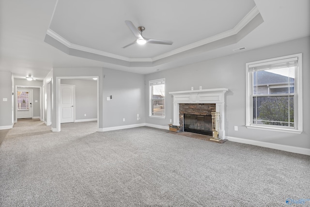 unfurnished living room with light carpet, a stone fireplace, ornamental molding, and a raised ceiling