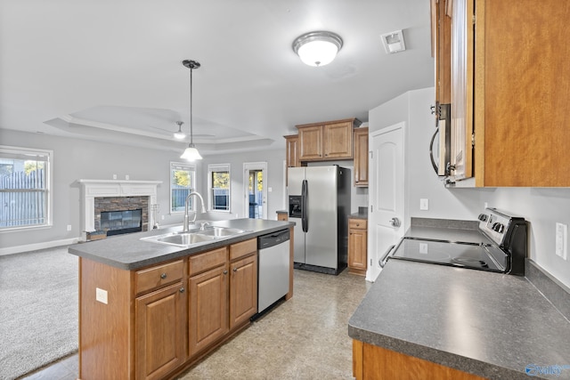 kitchen with sink, appliances with stainless steel finishes, a fireplace, an island with sink, and a raised ceiling