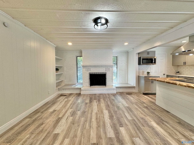 unfurnished living room with light hardwood / wood-style floors, wood walls, a fireplace, and ornamental molding