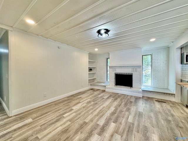 unfurnished living room featuring brick wall, built in features, a fireplace, and light hardwood / wood-style floors