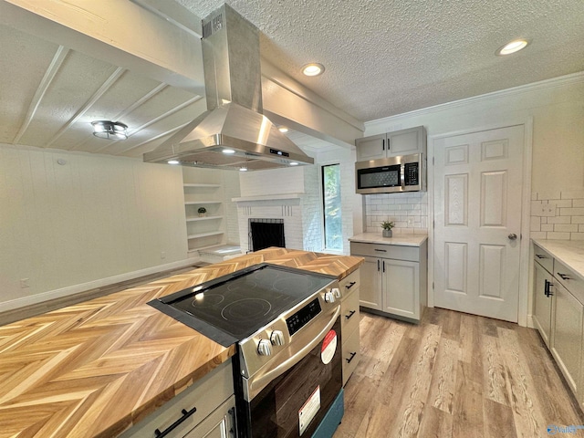 kitchen with appliances with stainless steel finishes, butcher block counters, backsplash, and range hood