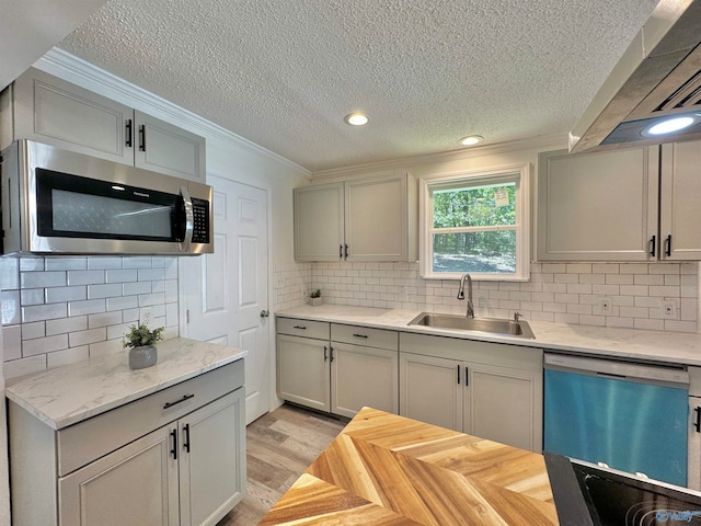 kitchen with backsplash, sink, crown molding, light wood-type flooring, and appliances with stainless steel finishes