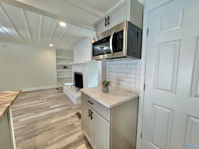 kitchen with light hardwood / wood-style flooring, backsplash, a brick fireplace, white cabinets, and light stone counters