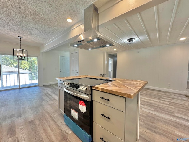 kitchen with island range hood, butcher block counters, stainless steel range with electric stovetop, hanging light fixtures, and light hardwood / wood-style floors