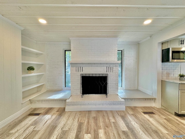 unfurnished living room with ornamental molding, built in features, a brick fireplace, and light wood-type flooring