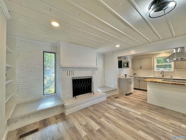 unfurnished living room with light hardwood / wood-style floors, crown molding, plenty of natural light, and a brick fireplace