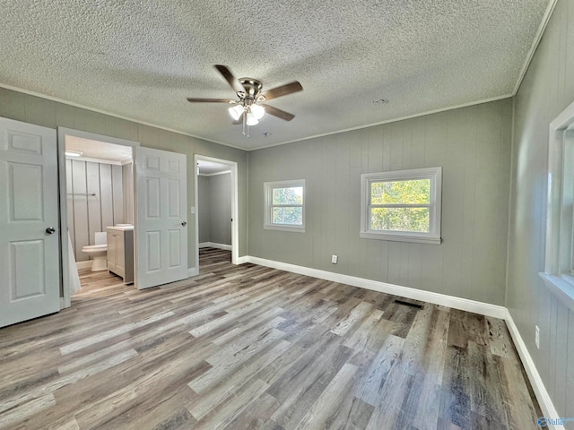 unfurnished bedroom featuring connected bathroom, light hardwood / wood-style flooring, ornamental molding, a textured ceiling, and ceiling fan