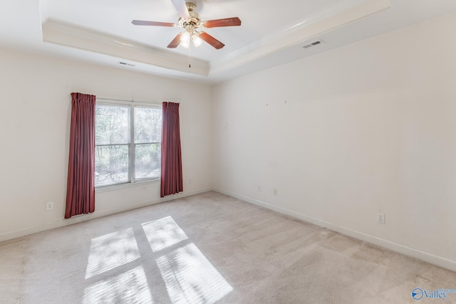 spare room featuring light carpet, ceiling fan, ornamental molding, and a tray ceiling