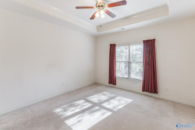 empty room featuring ceiling fan, crown molding, a tray ceiling, and light carpet