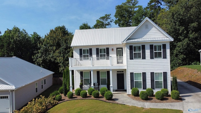 view of front of property with metal roof, a balcony, covered porch, driveway, and a front lawn