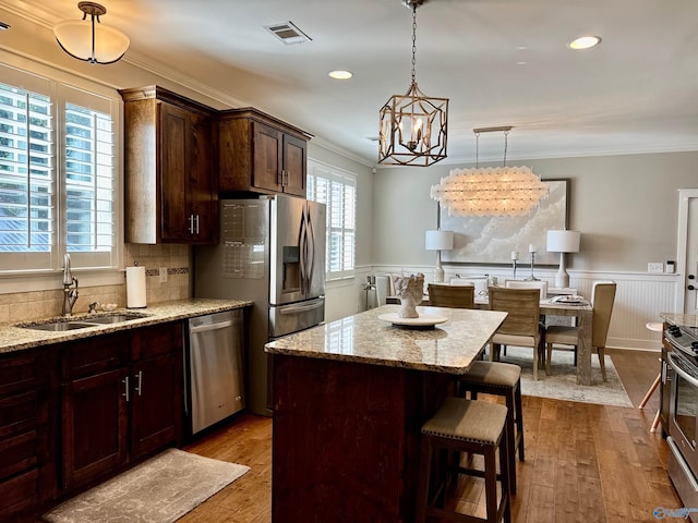 kitchen featuring crown molding, visible vents, appliances with stainless steel finishes, wainscoting, and a sink