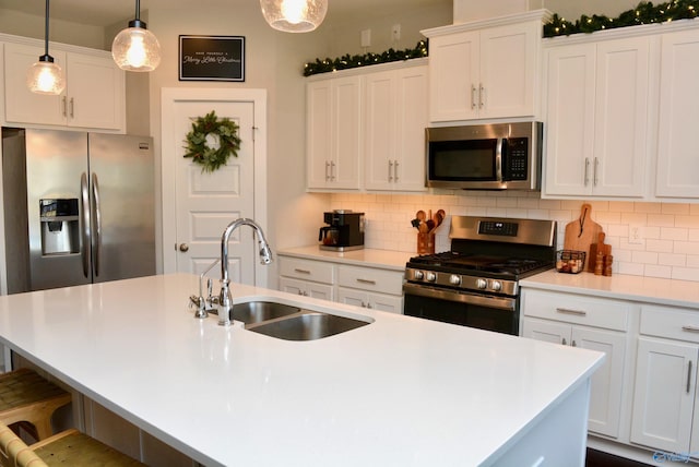 kitchen with decorative light fixtures, sink, appliances with stainless steel finishes, and an island with sink