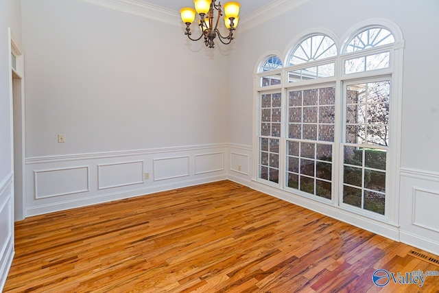 unfurnished room with visible vents, wainscoting, light wood-style flooring, an inviting chandelier, and crown molding