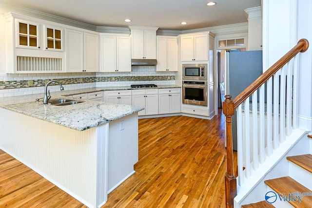 kitchen featuring light wood-style floors, a peninsula, stainless steel appliances, under cabinet range hood, and a sink