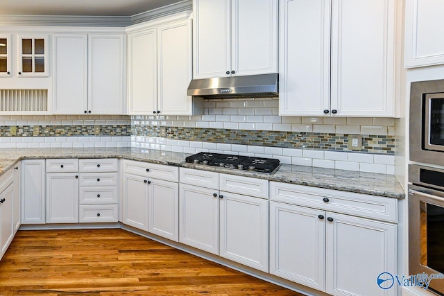 kitchen with under cabinet range hood, stainless steel appliances, white cabinets, light wood finished floors, and tasteful backsplash