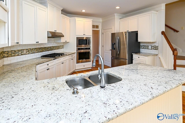 kitchen featuring decorative backsplash, appliances with stainless steel finishes, light stone countertops, under cabinet range hood, and a sink