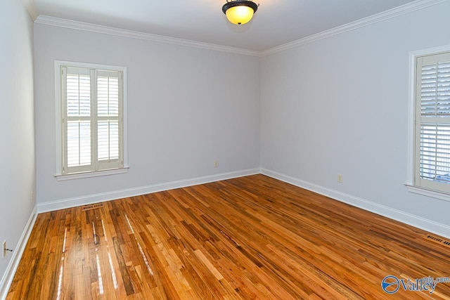 unfurnished room featuring wood-type flooring, visible vents, baseboards, and ornamental molding