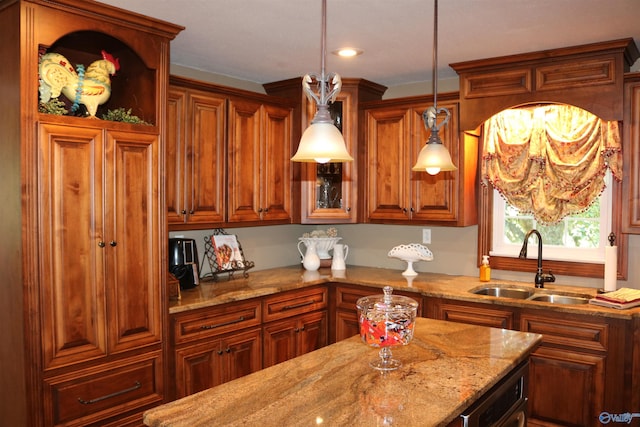kitchen featuring hanging light fixtures, brown cabinets, light stone countertops, and a sink