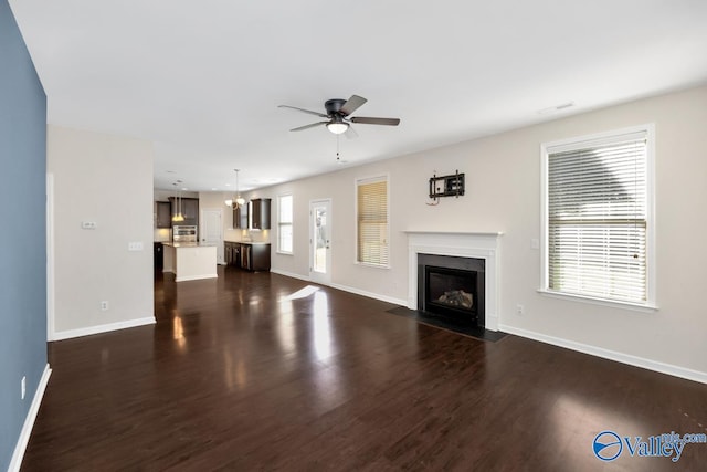 unfurnished living room featuring dark wood-type flooring, ceiling fan with notable chandelier, and a healthy amount of sunlight