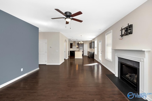 unfurnished living room featuring ceiling fan with notable chandelier and dark wood-type flooring