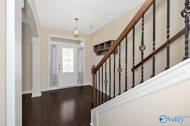 foyer featuring dark wood-type flooring, decorative columns, and a notable chandelier