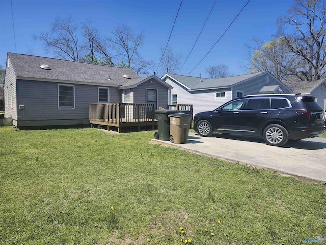 back of house with roof with shingles, a wooden deck, and a lawn