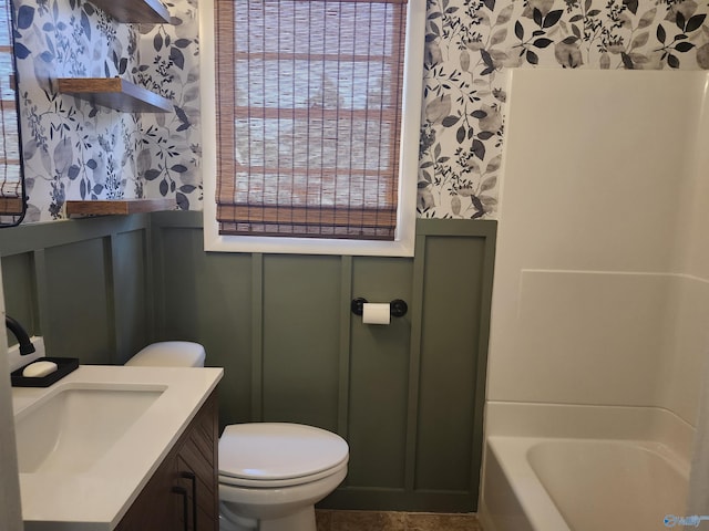 bathroom featuring wallpapered walls, toilet, a wainscoted wall, a tub to relax in, and a decorative wall