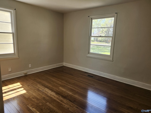 unfurnished room featuring baseboards, dark wood-style floors, and visible vents