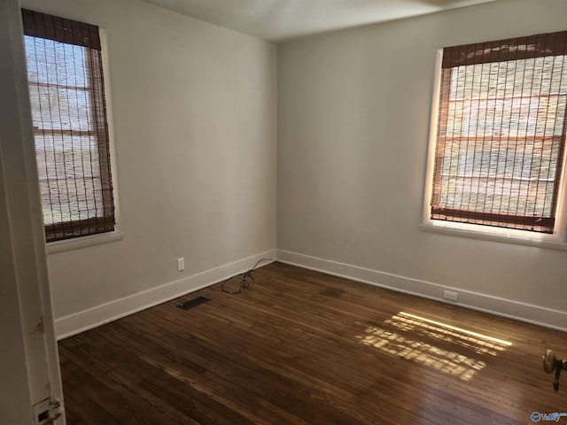 unfurnished room featuring dark wood-type flooring, visible vents, and baseboards