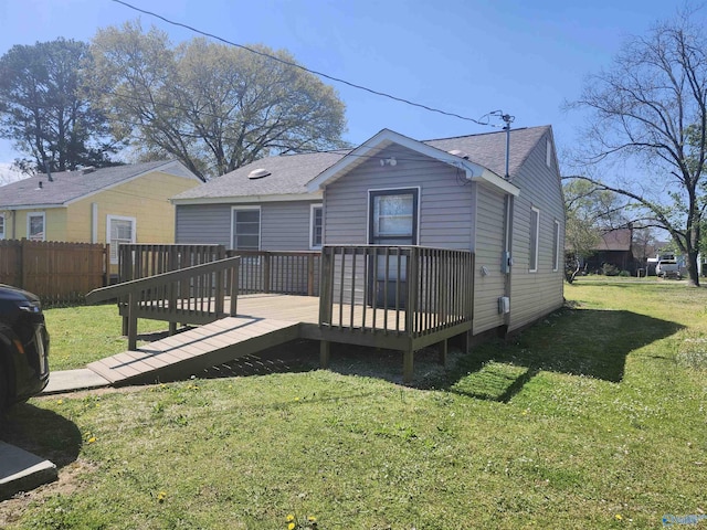 rear view of house with fence, a wooden deck, a lawn, and roof with shingles